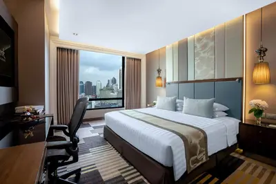 a hotel room with a bed and a desk and a window at The Landmark Bangkok in Bangkok