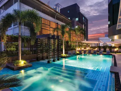 a swimming pool with palm trees in front of a building at Solitaire Bangkok Sukhumvit 11 in Bangkok