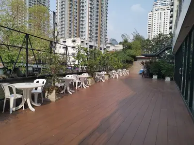 a wooden deck with white chairs and tables and buildings at Anya Nana at Sukhumvit Bangkok in Bangkok