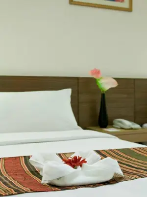 a bed with white sheets and a vase with flowers at The Seasons Bangkok Huamark in Bangkok