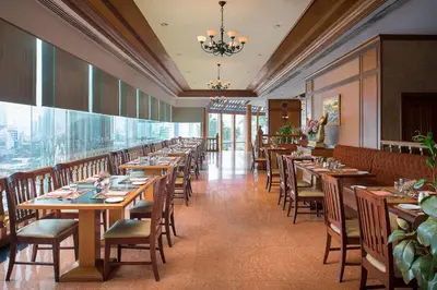 a restaurant with wooden tables and chairs and a large window at Prince Palace Hotel Bangkok in Bangkok