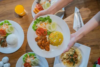 a person holding a plate of food on a table at Forum Park Hotel in Bangkok