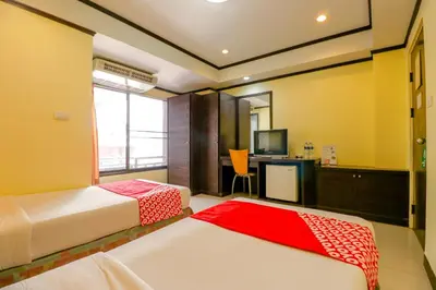 a bedroom with two beds and a desk with a television at Hotel Win Long in Bangkok