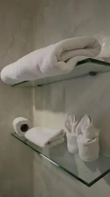 a glass shelf with towels and a roll of toilet paper at The Key Bangkok Hotel in Bangkok
