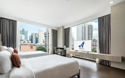 a hotel room with two beds and a large window at Adelphi Suites Bangkok in Bangkok