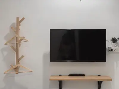 a flat screen tv on a wall with a wooden shelf at Click Hostel in Bangkok