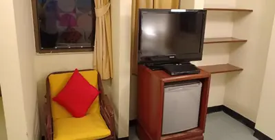 a room with a tv and a chair with a red pillow at Sawasdee Sukhumvit Inn in Bangkok
