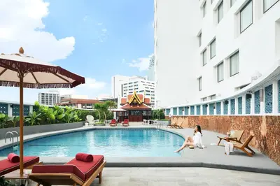 a woman is sitting next to a swimming pool at Montien Hotel Surawong Bangkok in Bangkok