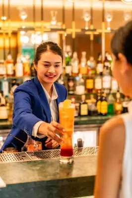 a woman standing at a bar with a drink at Montien Hotel Surawong Bangkok in Bangkok
