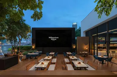a restaurant with tables and chairs and a projection screen at Millennium Hilton Bangkok in Bangkok