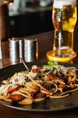 a plate of pasta on a table with a glass of beer at The Dawin Hotel in Bangkok