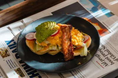 a black plate with a sandwich with bacon and vegetables at The Dawin Hotel in Bangkok