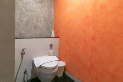 a bathroom with a toilet and an orange wall at Zleepmotion Bangkok in Bangkok