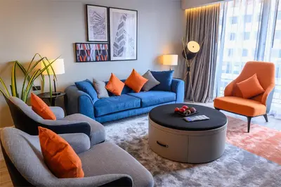 a living room with blue couches and orange chairs at Oakwood Residence Sukhumvit Thonglor Bangkok in Bangkok