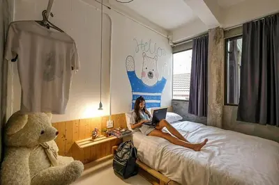 a woman sitting on a bed with a laptop at Pastelhouse hostel in Bangkok