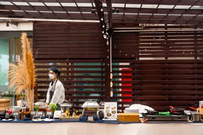a person wearing a mask behind a table with food at Amanta Hotel & Residence Ratchada in Bangkok