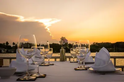 a table with wine glasses and a sunset in the background at Kalanan Riverside Resort in Nonthaburi