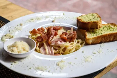 a plate of food with pasta and bacon and bread at Khaosan Art Hotel in Bangkok