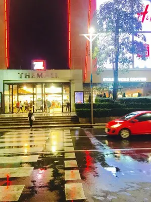 a red car driving past a store at night at Mall Suites Hotel in Bangkok