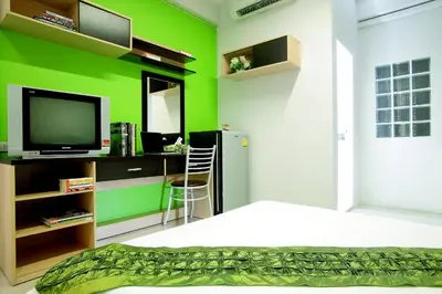 a room with a green wall with a television and a desk at Smile Inn in Bangkok