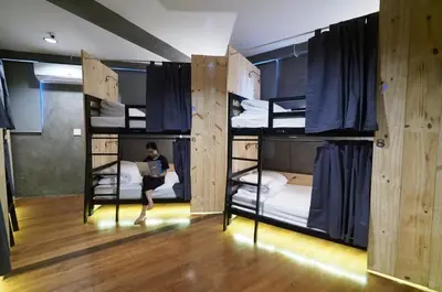a person sitting on a laptop in a room with bunk beds at Luck Yimm Hostel in Bangkok