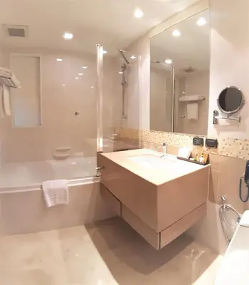a bathroom with a sink and a tub and a mirror at Amora NeoLuxe Suites Hotel in Bangkok