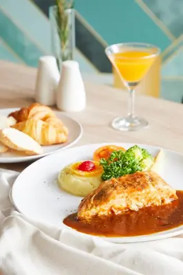 a table with two plates of food and a glass of orange juice at The Quarter Ladprao by UHG in Bangkok
