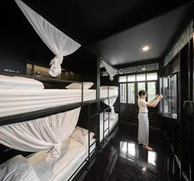 a woman standing in a room with four bunk beds at Kloem Hostel in Bangkok