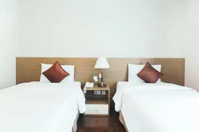 two beds in a hotel room with white sheets at Thomson Residence Hotel in Bangkok