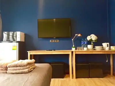 a room with a table with a television on a blue wall at My Home N1 - BTS Ratchathewi in Bangkok