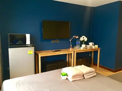 a room with a desk with a television and a table with towels at My Home N1 - BTS Ratchathewi in Bangkok