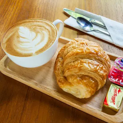 a tray with a cup of coffee and a croissant at At Hua Lamphong Hotel in Bangkok