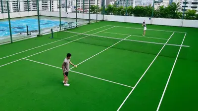 two people playing tennis on a green tennis court at Grande Centre Point Hotel Terminal21 in Bangkok