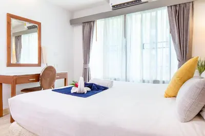 a bedroom with a large white bed with a desk and a mirror at Lasalle Suites Hotel & Residence in Bangkok