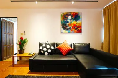 a black leather couch in a living room with a painting at Serena Sathorn Suites in Bangkok