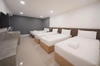 a room with four beds with white sheets and a counter at Grand Alpine Hotel in Bangkok
