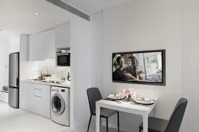 a white kitchen with a table and a tv on a wall at Somerset Maison Asoke Bangkok in Bangkok