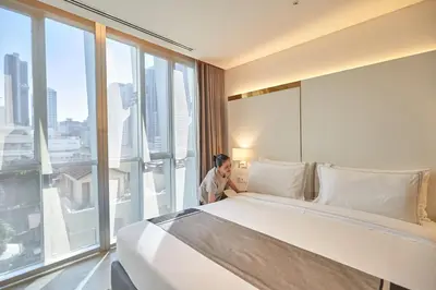 a woman standing next to a large bed in a hotel room at Somerset Maison Asoke Bangkok in Bangkok