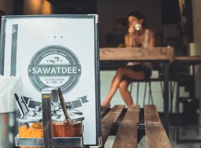 a woman sitting at a table in a restaurant with a sign at Sawatdee Guesthouse the Original in Bangkok