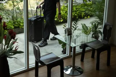 a man with a suitcase and a glass table and chairs at Nantra Silom in Bangkok