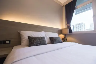 a bedroom with a white bed with pillows and a window at Maxim's Inn in Bangkok