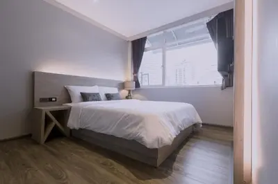 a white bedroom with a bed and a window at Maxim's Inn in Bangkok