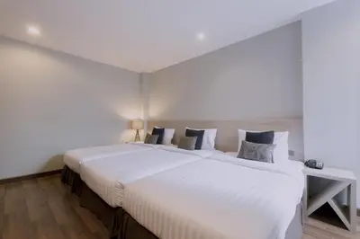 a large white bed in a room with a table at Maxim's Inn in Bangkok