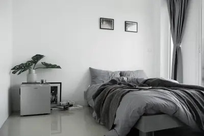 a white bedroom with a bed and a potted plant at Studio 41 Salaya-Sai4 in Nakhon Pathom
