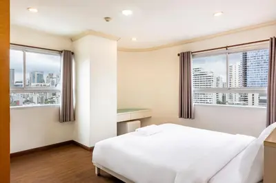 a bedroom with a white bed and two windows at Teja Hotel in Bangkok