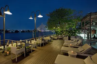 a deck with white chairs and tables and a body of water at Riva Surya Bangkok in Bangkok