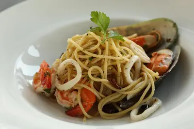 a white plate of pasta with shrimp and vegetables at Riva Surya Bangkok in Bangkok
