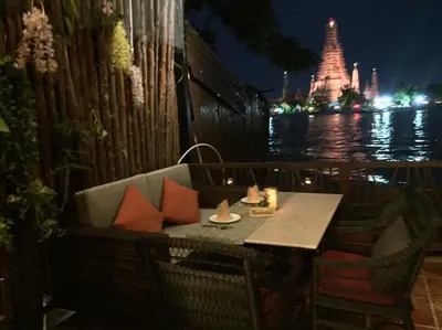 a table and chairs on a balcony near the water at night at Sala Arun in Bangkok