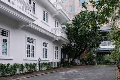 a white building with a tree in front of it at Baan Vajra in Bangkok
