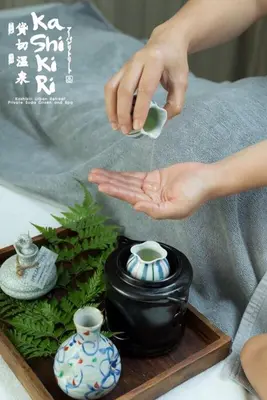 a person holding a cup in front of a vase at MAYU Bangkok Japanese Style Hotel in Bangkok